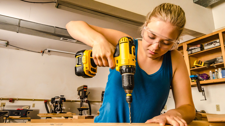 Young woman using DeWalt power drill on wood board