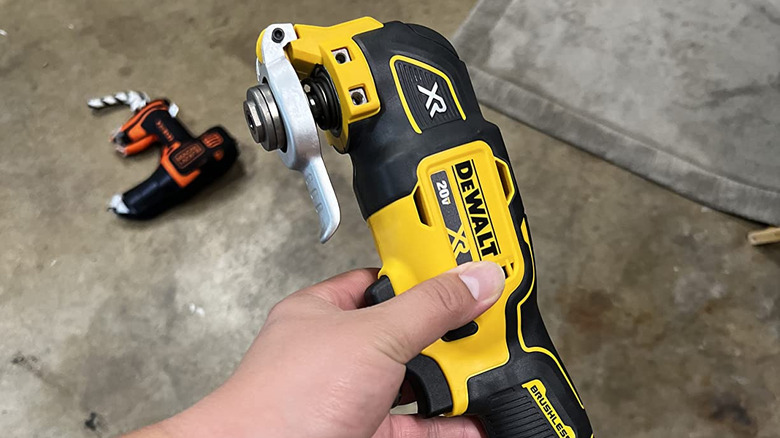 Hand holding new DeWalt oscillating multi-tool above dirty garage floor with fallen tools