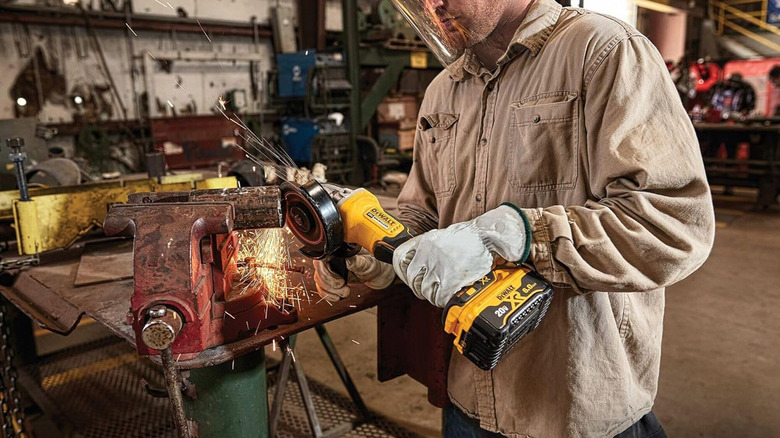 Man operating angle grinder on metal in large garage with various tools