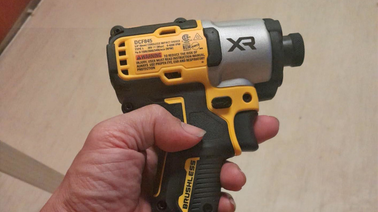 Man holding DeWalt impact driver above wood material