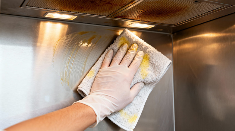 A hand wiping down a greasy stainless steel range hood