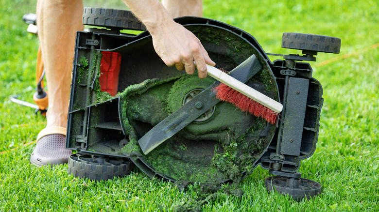 A person cleaning the blades of their lawn mower
