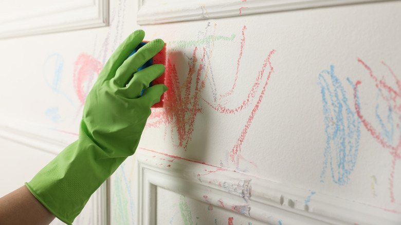 A young child drawing on a wall with crayon