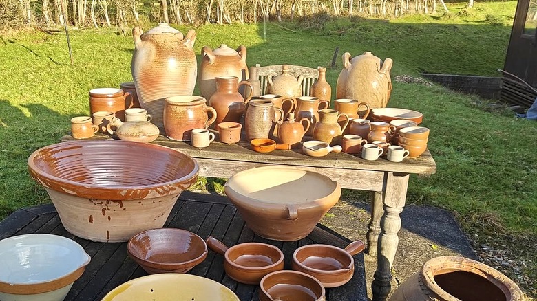 A collection of antique jugs, pots, and bowls on wooden tables in a sunny garden.