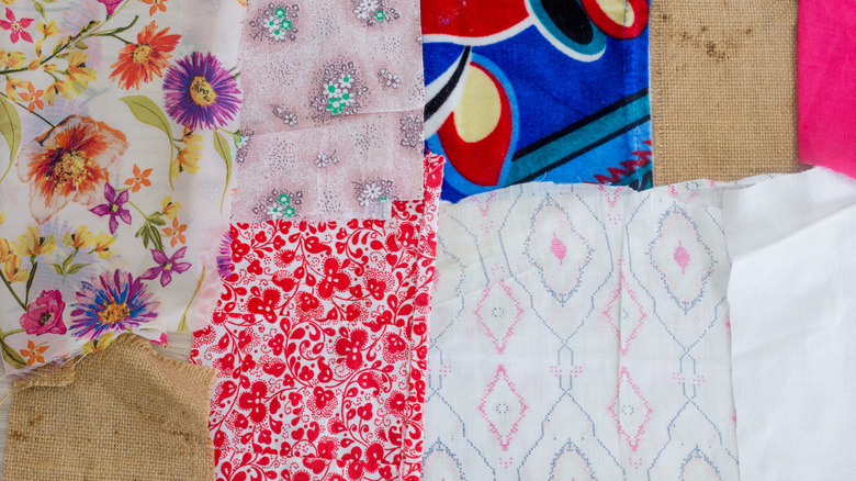 Various colorful fabric pieces, threads, lace, and buttons arranged for patchwork crafting and creative textile recycling on a wooden surface.