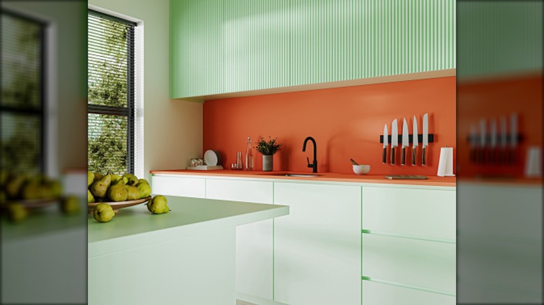 A kitchen with a clay-colored backsplash and mint green, fluted cabinets.