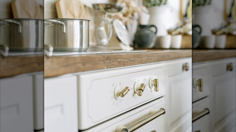 A close up of appliances and kitchen cabinets with brass fixtures and hardware.