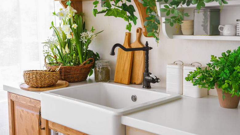 A close up of a farmhouse sink with white quartz countertops and a curved faucet.