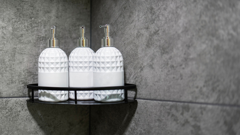 A corner shower caddy with white bottles of soap or shampoo stored on it