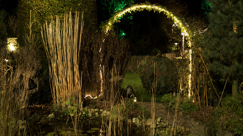 A metal garden arch covered in yellow, pink, and green LED rope lights.