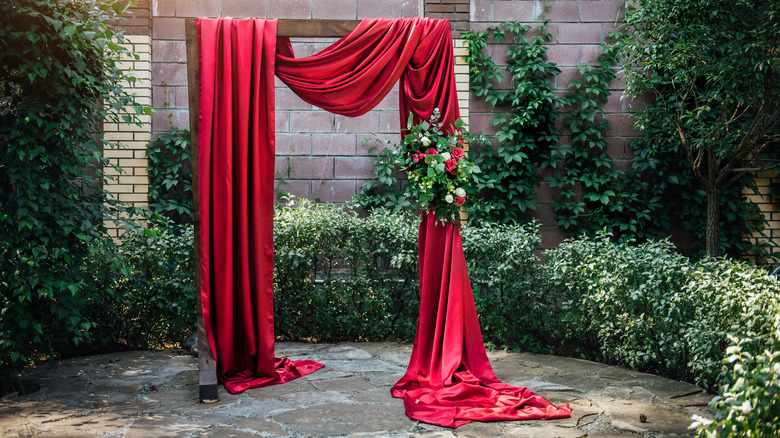 Red fabric draped on wooden garden arch.