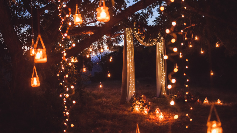 Candles in jars hanging from arch with fairy lights