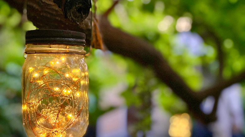 Close up of a mason jar with string lights inside hanging on a tree branch