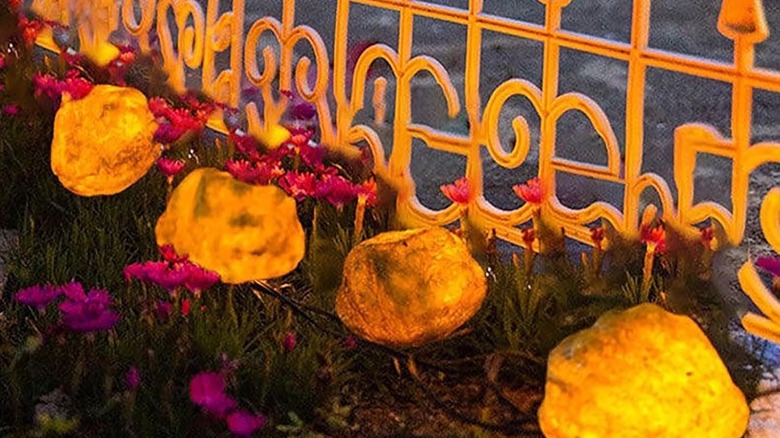 Solar-powered light-up rocks sitting next to flowers and a decorative fence