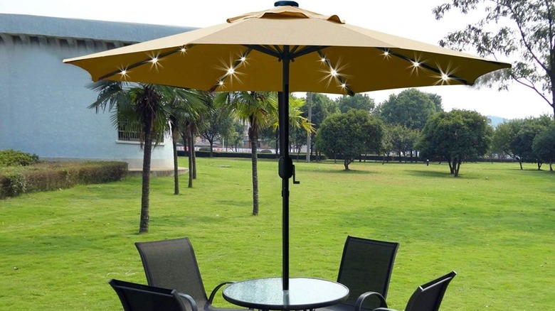 A tan patio umbrella with lights built into the under side installed over a four-person table in a yard