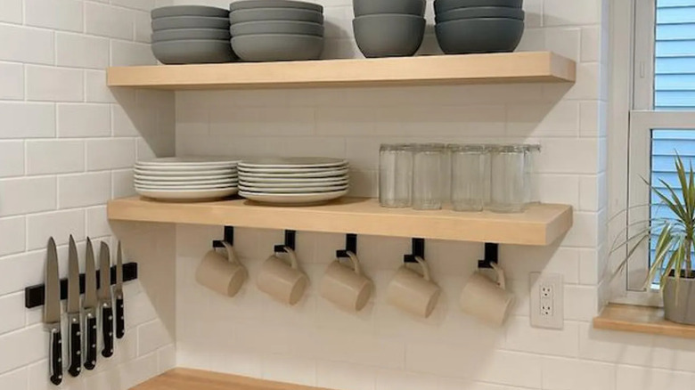 mugs hanging on hooks from an open shelf stacked with plates and glasses