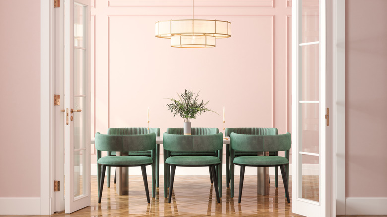 A formal dining room with pink walls and six green upholstered chairs