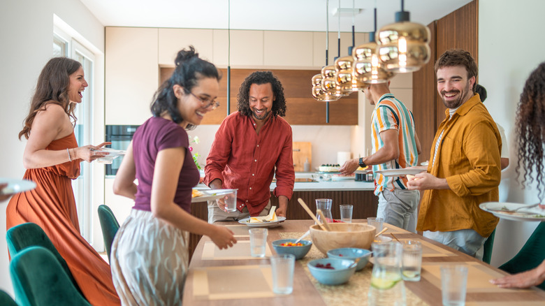 A diverse group of friends clean up a dining room table after a meal