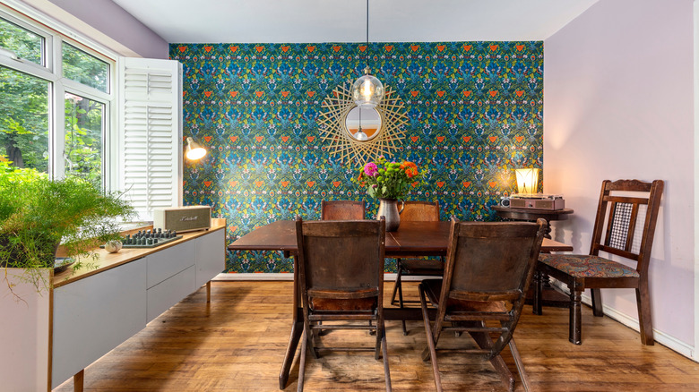 A fining room with one accent wall covered in a teal-patterned wallpaper