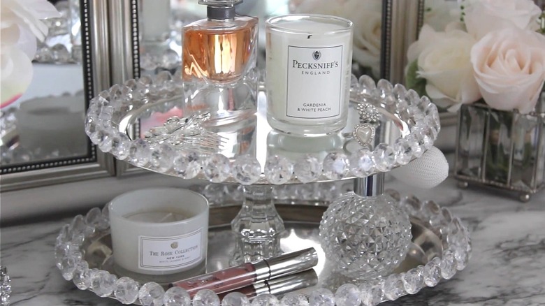 Two-tier vanity stand with gemstones along the edge and candles and cosmetics on the trays