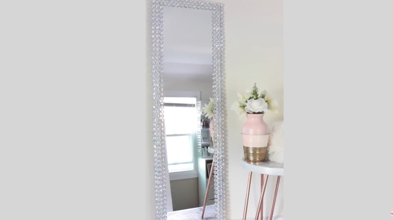 Full-length mirror with clear gems covering the frame next to a small table
