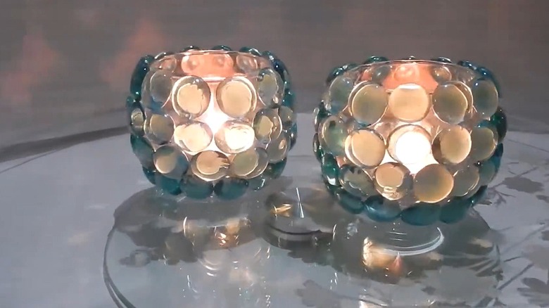 Two rounded candleholders covered with gems with candles glowing inside