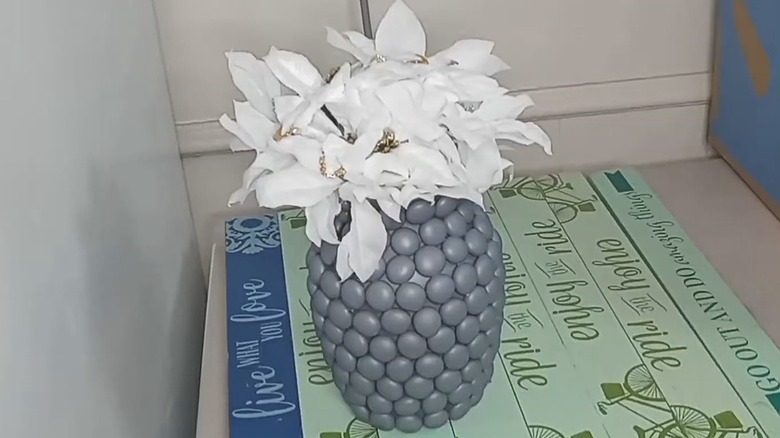 Glass vase covered in gems and spray painted with white silk flowers sticking out of the top