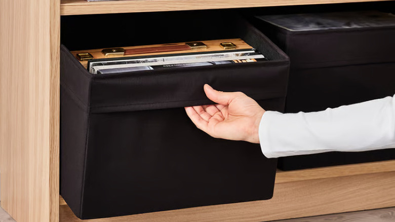 Woman pulling black box off shelf filled with documents and books