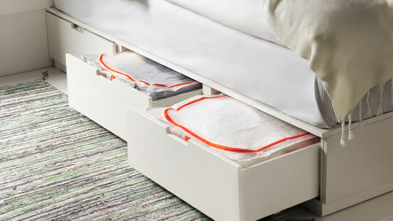Bed frame with drawers and white storage bags filled with bedroom items