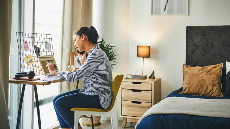 Woman browsing computer and on phone in organized mid-century modern bedroom