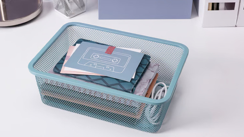 Blue mesh metal desktop organizer filled with notebooks and cards on white desk