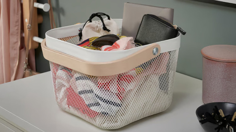 Cute mesh basket with wood handle filled with wallet, fabric, and various bedrooom items on white table