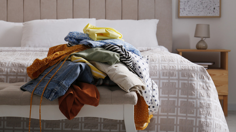 pile of dirty cloth on bench at the foot of a bed