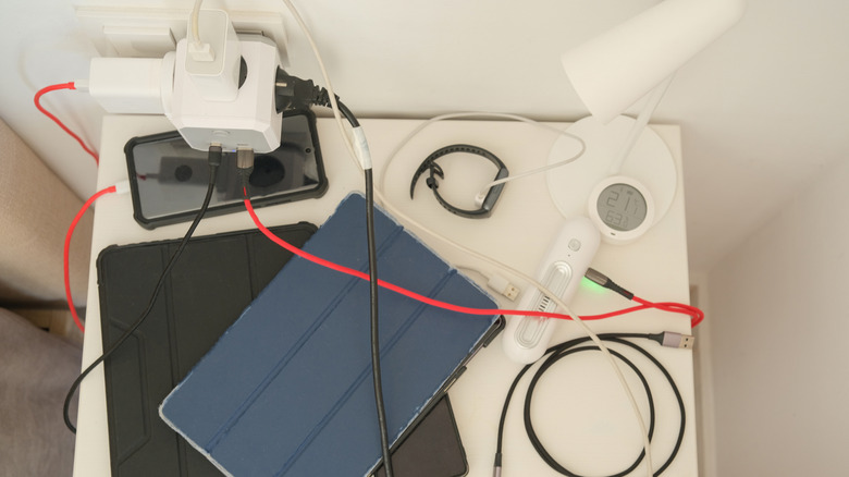 multiple devices and cables connected to a power outlet on a nightstand