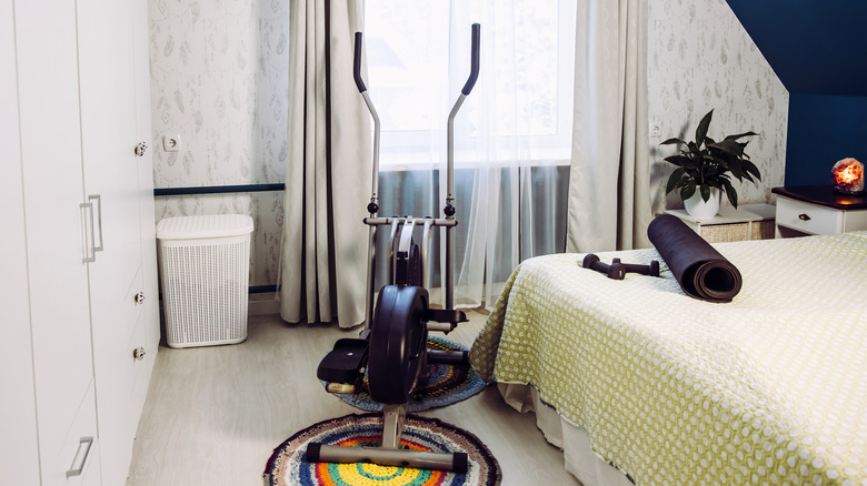 elliptical in bedroom with yoga mat and weights n the bed