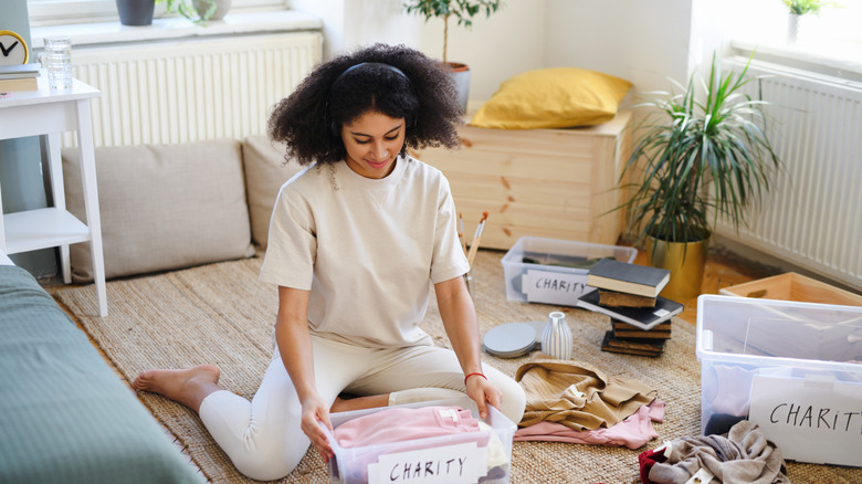 lady sitting on the floor in bedroom and organizing items to donate to charity