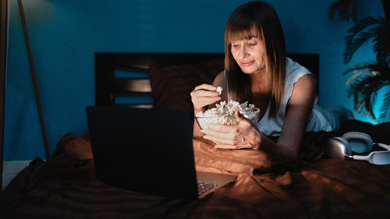 lady eating popcorn while watching a movie on her laptop in a bedroom at night
