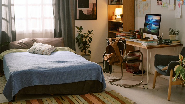 bedroom with workspace on one side with clutter of books and other materials on the table