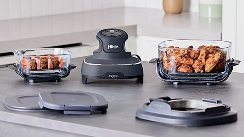 An air fryer sits on top of a gray table with containers of food next to it.