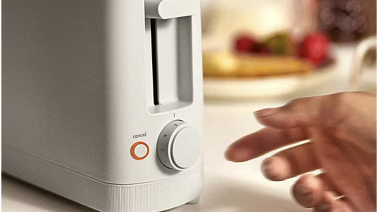 A hand reaches to turn the dial on a toaster.