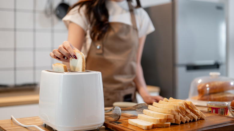 A woman using a toaster with toasted bread on the table