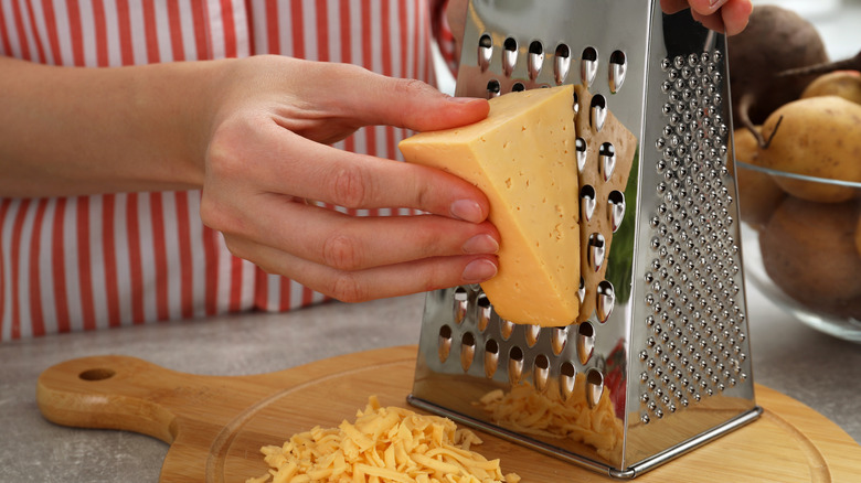 Person grating cheese with a stainless steel box cheese grater