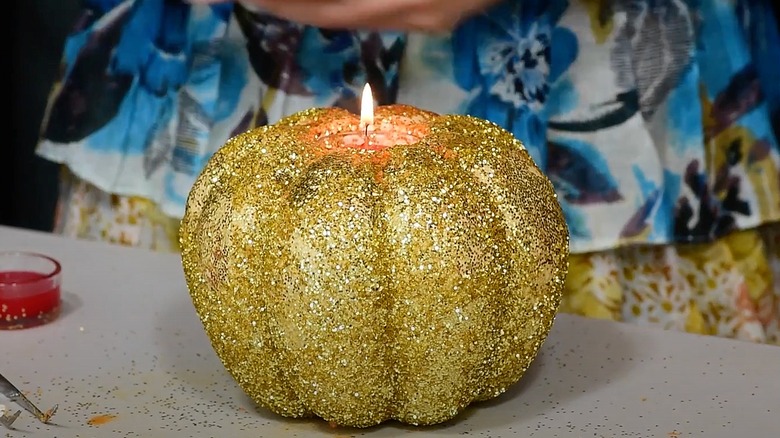 A glitter-covered carved pumpkin with a lit wax candle inside