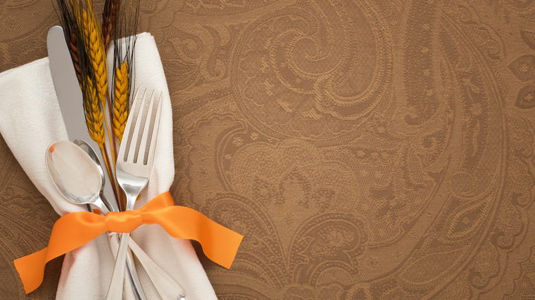 Napkin and silverware tied with orange ribbon and wheat