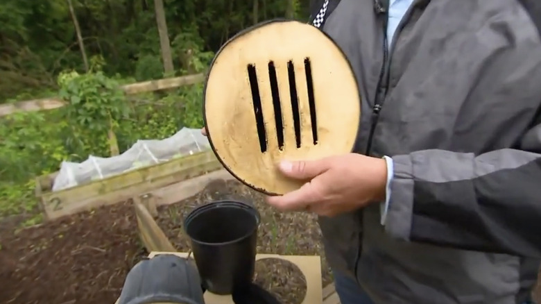 A man holds a butterfly house made from an old plastic nursery pot and a piece of slatted wooden board.