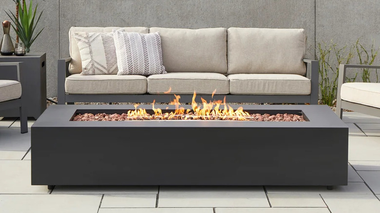 Real Flame Monaco 70-inch Rectangle Steel Fire Pit Table with Patio Furniture and a Gray Wall