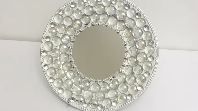 Decorative mirror with a charger as the frame covered in gemstones and hanging on a white wall