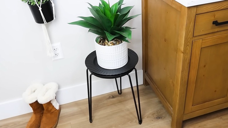 Black plant stand with a decorative charger on top and a potted plant displayed