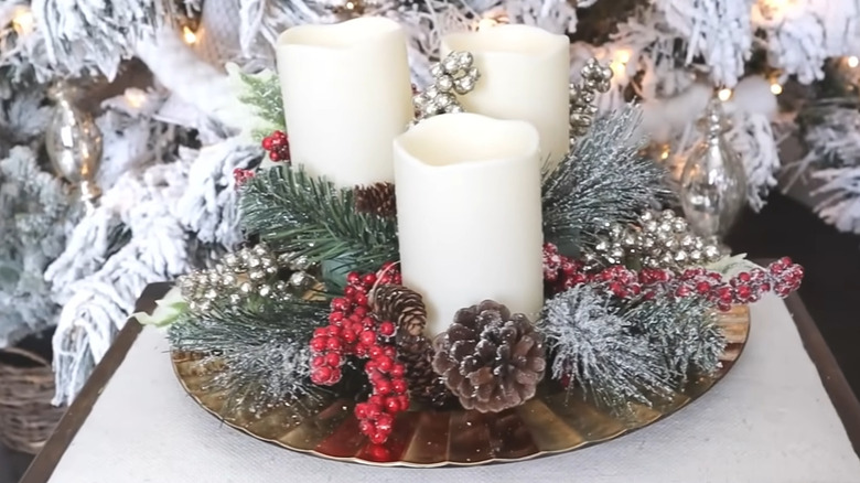 Candles, pine boughs, pine cones, and berries on a charger