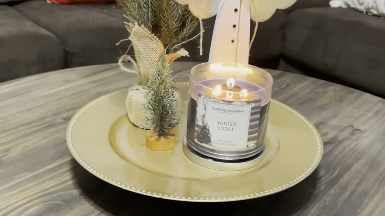 Side view of a gold charger with feet added to elevate the display with a candle and tree on top